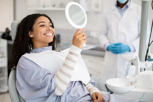 Smiling dental patient sitting in dental exam chair and looking in mirror with implant supported bridge at Lakewood Dental Arts in Lakewood, CA