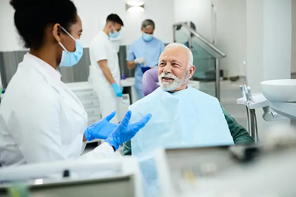 Older patient sitting in dental chair calmly discussing his oral health with his female dentist at Lakewood Dental Arts in Lakewood, CA