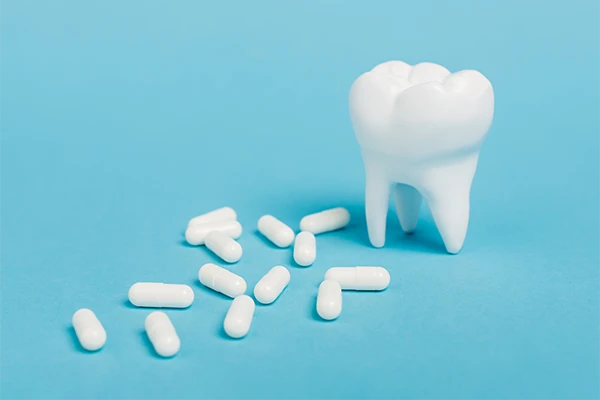 3D-printed tooth sitting on a blue background next a scattered number of plain, white pills illustrated by Lakewood Dental Arts in Lakewood, CA