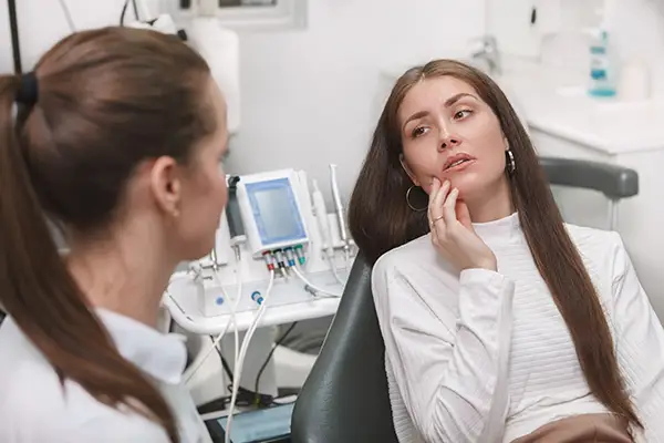 A woman touching her jaw while discussing TMJ pain and treatment options, such as Botox, with a specialist.