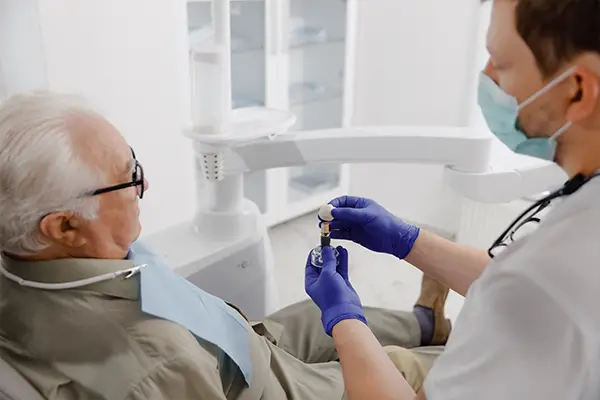 A dentist explains the dental implant process to an older patient with implant tooth model at Lakewood Dental Arts in Lakewood, CA
