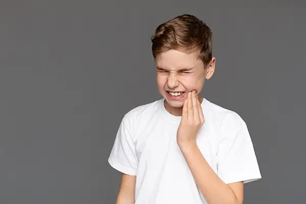 Young boy grimacing in pain while holding his jaw, indicating a dental emergency at Lakewood Dental Arts in Lakewood, CA